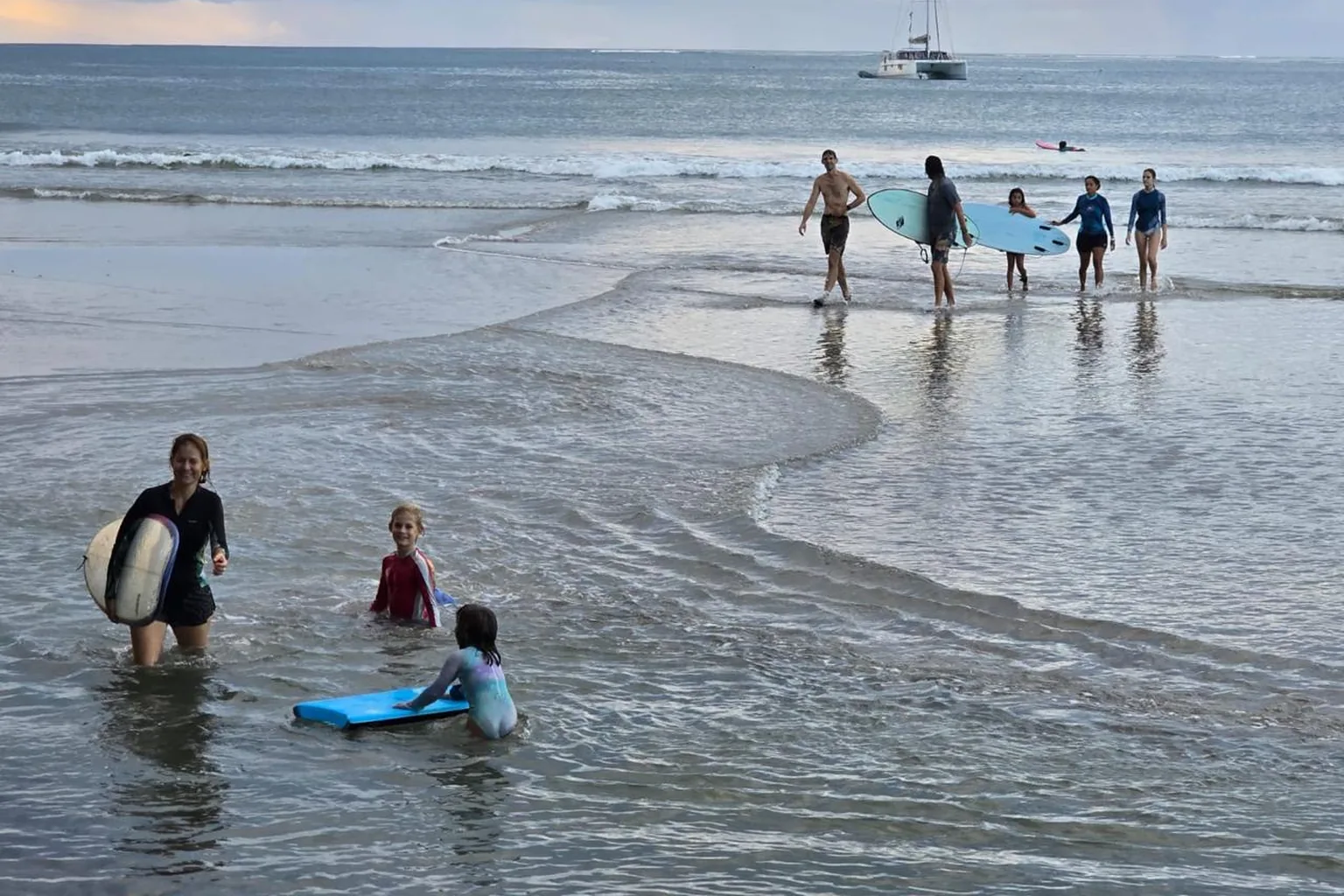 A parent wades into the shallows with a board while Duckies play in the water behind.